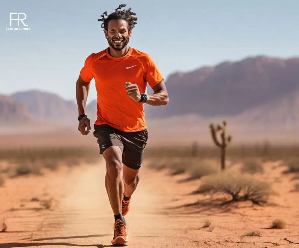 An energetic young man running in the desert while wearing orange running shirt, brown running shorts & matching running shoes.