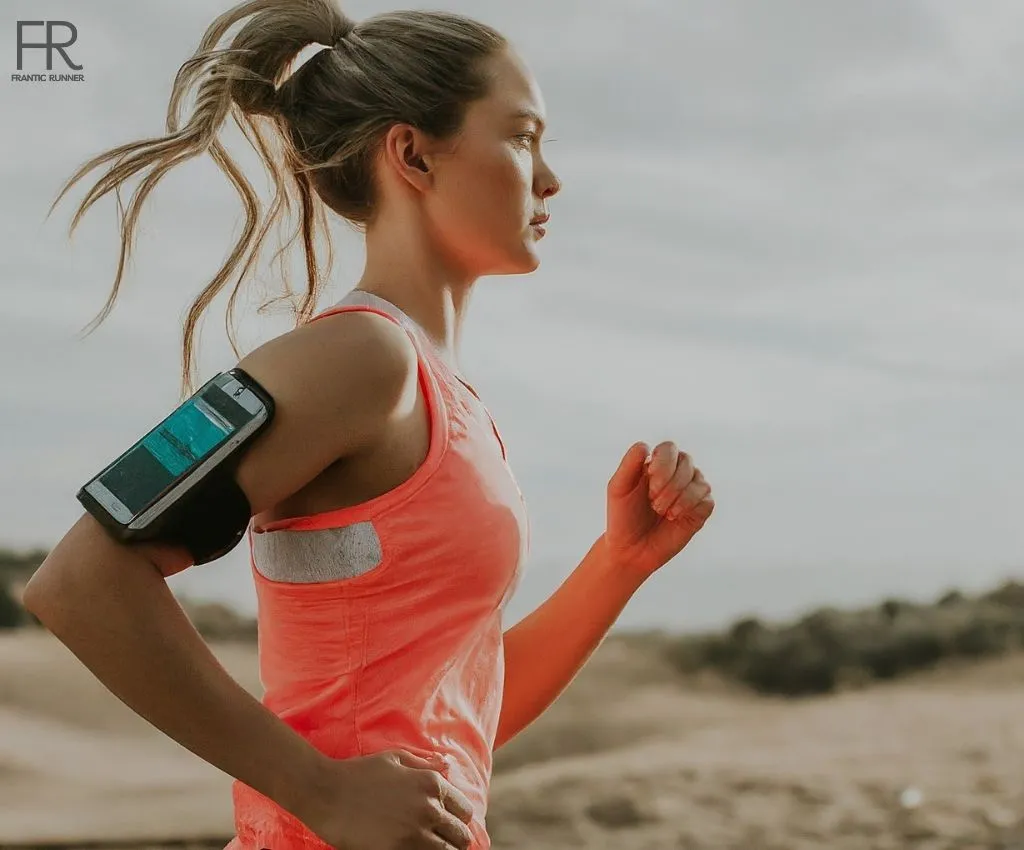 an energetic female runner running while securing her phone safely in the armband wrapped around the upper arm