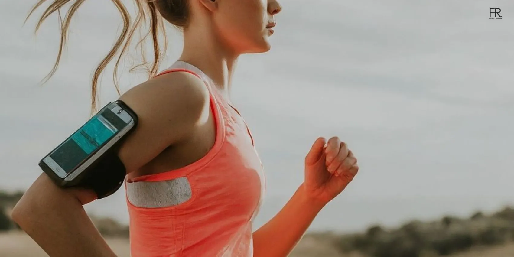 an image of an energetic female runner running while securing her phone safely in the armband wrapped around the upper arm