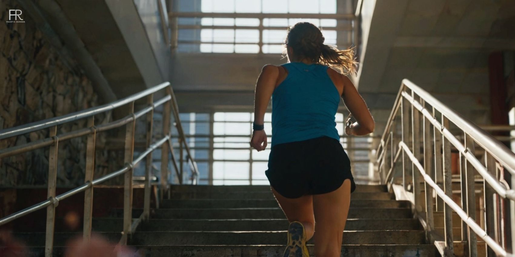 an female runner running on the stairs while wearing running t-shirt, shoes & short running shorts